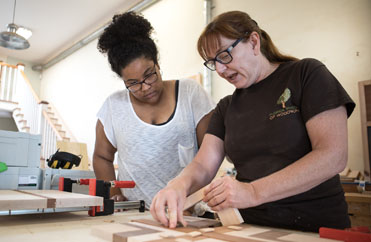 Female woodworking instructor teaches student during class
